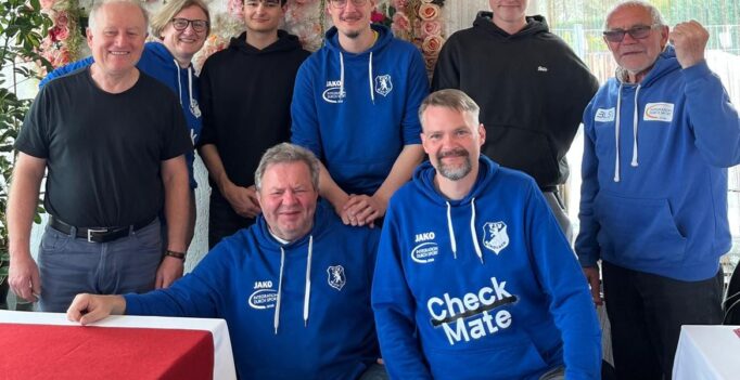 Group photo of eight people wearing blue hoodies, posing in front of a floral backdrop with 'La Familia' sign.