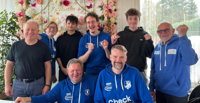 Nine people smile for a group photo in front of a colorful flower wall with 'La Familia' script.
