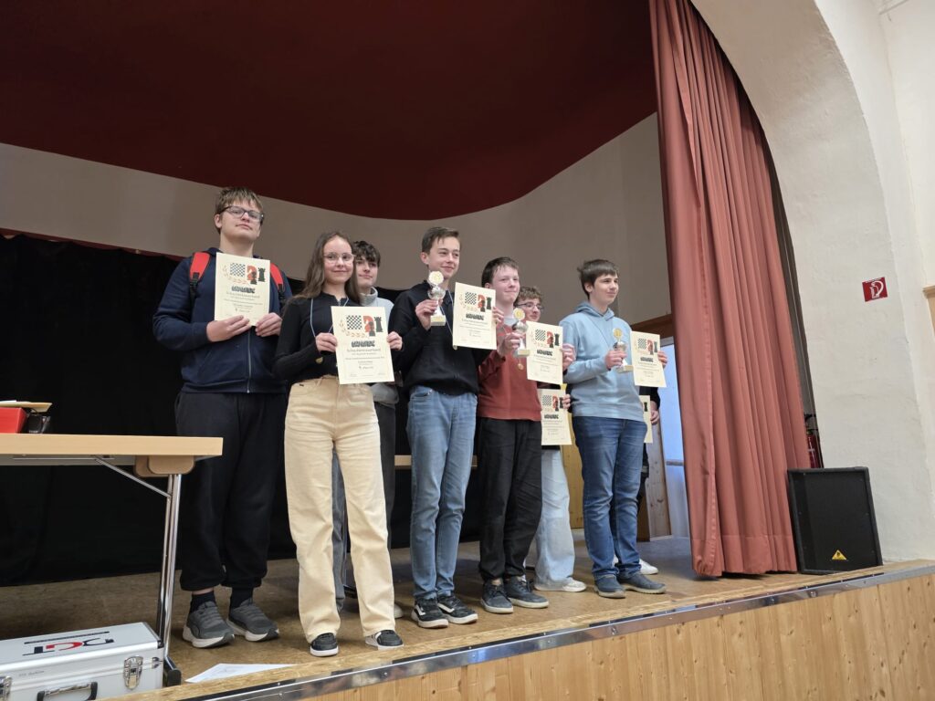 Group of smiling teens on a stage holding certificates and trophies after an awards ceremony.
