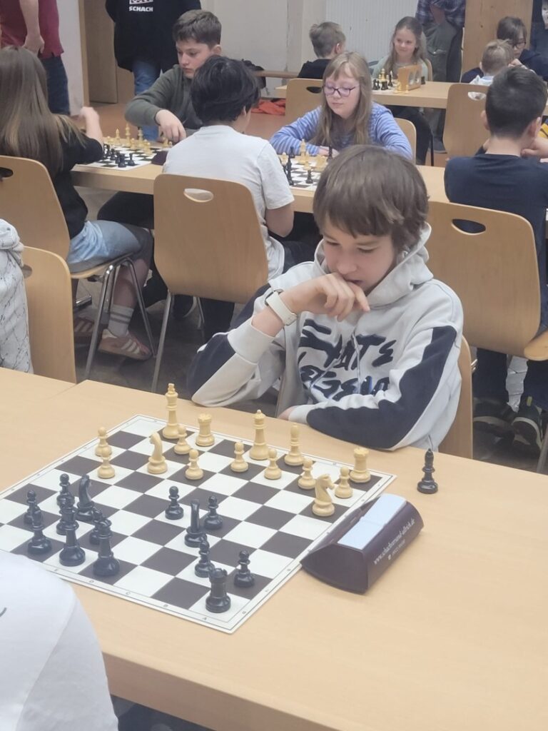 Boy in a gray hoodie deeply thinking at a chessboard during a kids' chess tournament.
