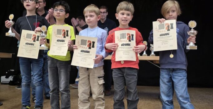 Five young boys stand on a stage holding certificates and trophies from an awards ceremony, posing for a group photo.