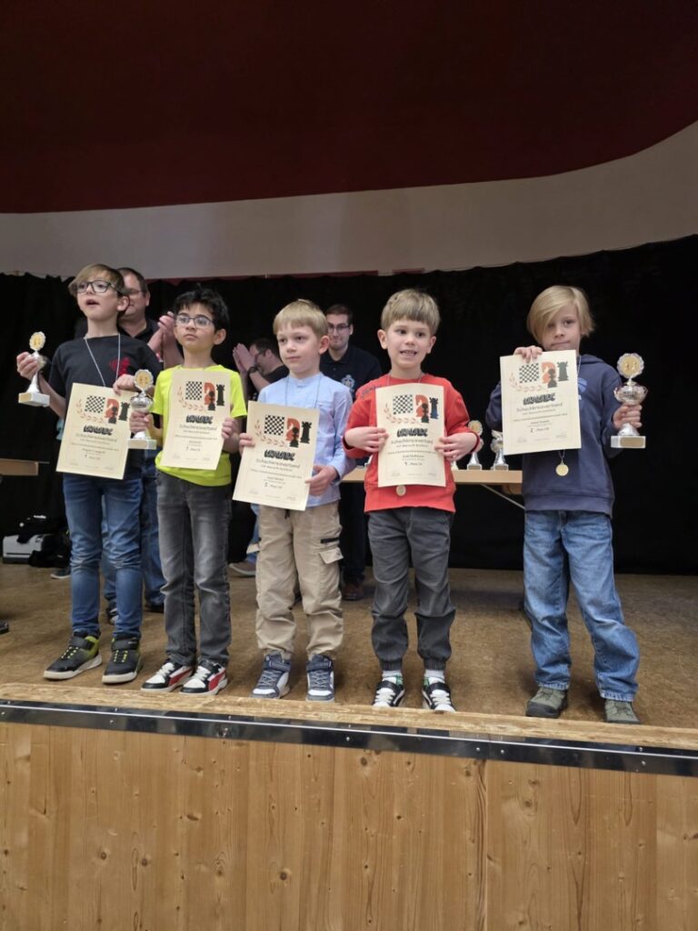Five young boys stand on a stage holding certificates and trophies from an awards ceremony, posing for a group photo.