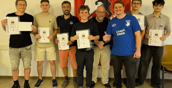 Group photo of eight men indoors, each holding certificates, standing in front of a red and white banner with a black lion emblem (award ceremony).